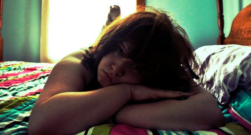 Teenage girl lying on her stomach on her bed, upset