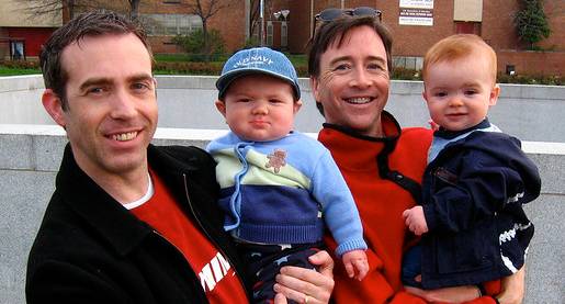 two men both holding infant children