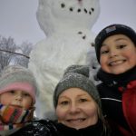 Shelly VanBuren smiling with her young granddaughter and grandson in front of a snowman