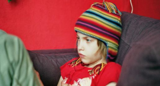 Adolescent child sitting on a couch with knees up and wearing a winter hat