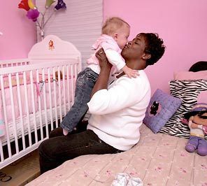 Black adoptive mother kisses her white toddler in a pink child's bedroom